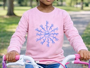 A young girl in a pink sweater holding a bicycle with pink handles.